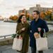 Newcomer couple walking along Canadian harbourfront promenade with fresh groceries near apartment buildings and port cranes